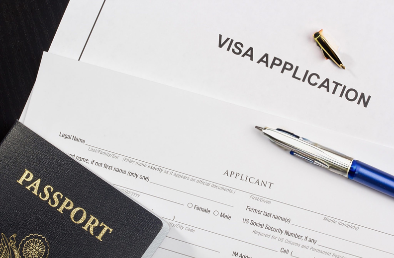 A visa application form, a passport, and a pen placed on a desk.