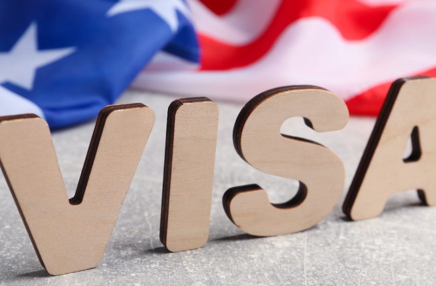 Wooden letters spelling 'Visa' on a desk with a United States flag in the background.