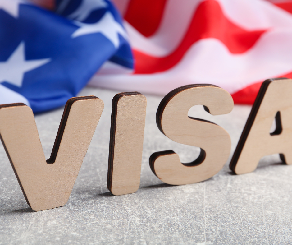 Wooden letters spelling 'Visa' on a desk with a United States flag in the background.